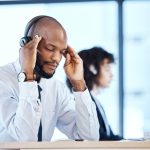 Employé assis à son bureau, les mains sur le visage, visiblement accablé par le stress.