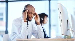 Employé assis à son bureau, les mains sur le visage, visiblement accablé par le stress.
